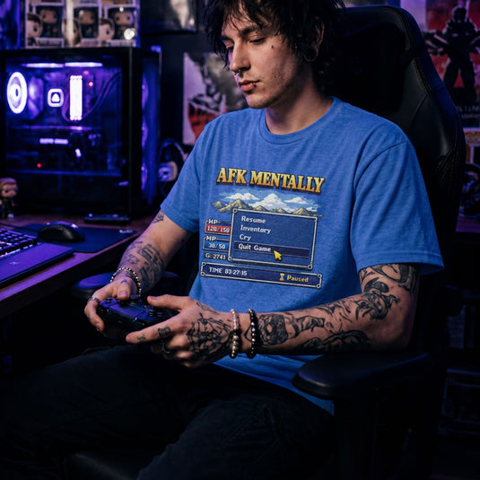Translation missing: en.Heather royal tee with gold AFK Mentally text over a pixel art retro RPG menu box with a cursor hovering on Quit Game