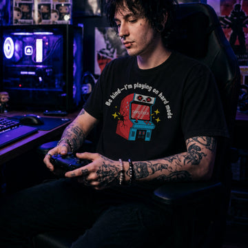 Translation missing: en.Black shirt with text Be kind—I'm playing on hard mode above a cracked retro arcade cabinet with Game Over