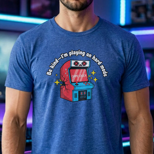 Translation missing: en.Heather royal shirt with text Be kind—I'm playing on hard mode above a cracked retro arcade cabinet with Game Over