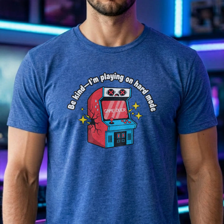 Translation missing: en.Heather royal shirt with text Be kind—I'm playing on hard mode above a cracked retro arcade cabinet with Game Over