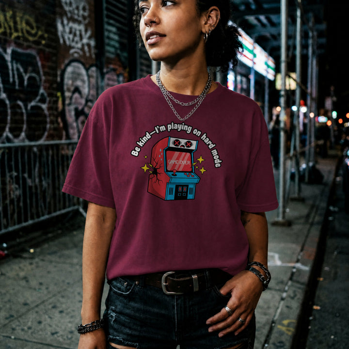 Translation missing: en.Maroon shirt with text Be kind—I'm playing on hard mode above a cracked retro arcade cabinet with Game Over