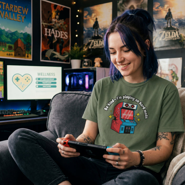Translation missing: en.Military green shirt with text Be kind—I'm playing on hard mode above a cracked retro arcade cabinet with Game Over