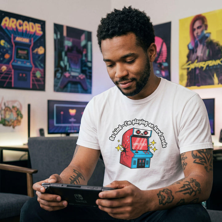 Translation missing: en.White shirt with text Be kind—I'm playing on hard mode above a cracked retro arcade cabinet with Game Over