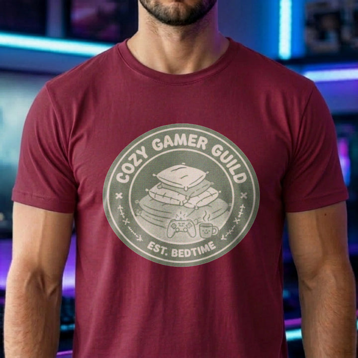 Translation missing: en.Cardinal red t-shirt with a green badge showing stacked pillows, a controller, and text Cozy Gamer Guild Est. Bedtime