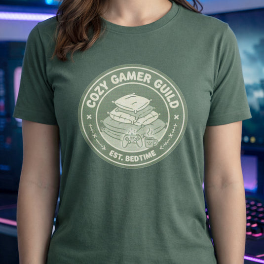 Translation missing: en.Military green t-shirt with a green badge showing stacked pillows, a controller, and text Cozy Gamer Guild Est. Bedtime
