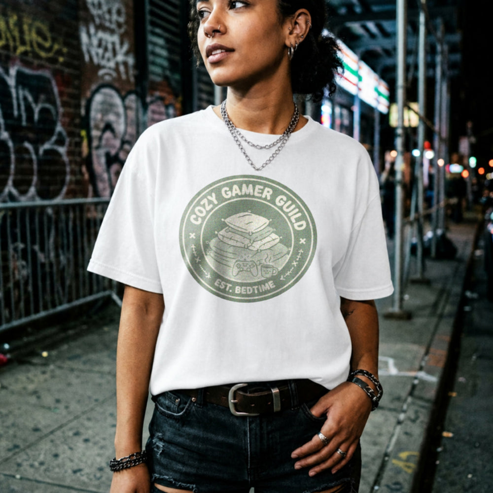 Translation missing: en.Alt n Vibe white t-shirt with a green badge showing stacked pillows, a controller, and text Cozy Gamer Guild Est. Bedtime
