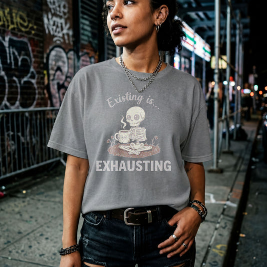 Translation missing: en.White text Existing is Exhausting around a cute skeleton sitting cross legged holding a skull coffee mug on graphite heather tee