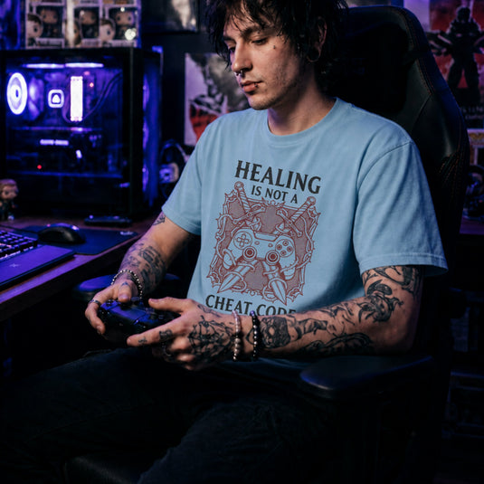 Translation missing: en.Light blue gamer tee graphic with crossed swords, controller, and thorns text Healing Is Not A Cheat Code. 