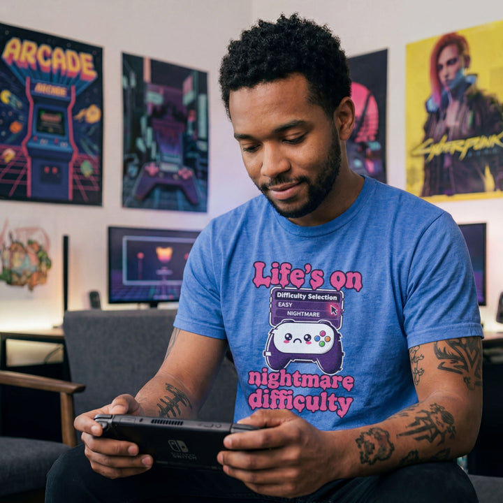 Translation missing: en.Heather royal tee with pink text reading Life's on nightmare difficulty next to a sad controller and difficulty selector