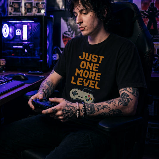 Translation missing: en.Retro black t-shirt with orange pixelated text reading Just One More Level above a classic retro game controller
