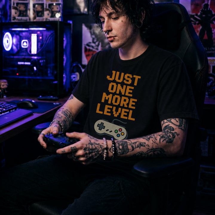 Translation missing: en.Retro black t-shirt with orange pixelated text reading Just One More Level above a classic retro game controller