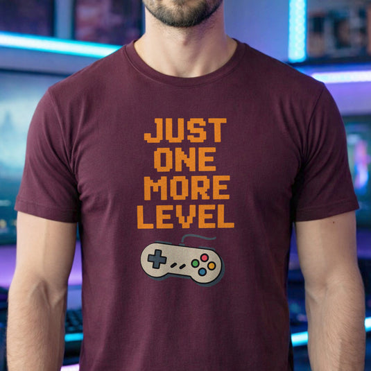 Translation missing: en.Retro maroon t-shirt with orange pixelated text reading Just One More Level above a classic retro game controller