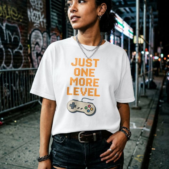 Translation missing: en.Retro white t-shirt with orange pixelated text reading Just One More Level above a classic retro game controller