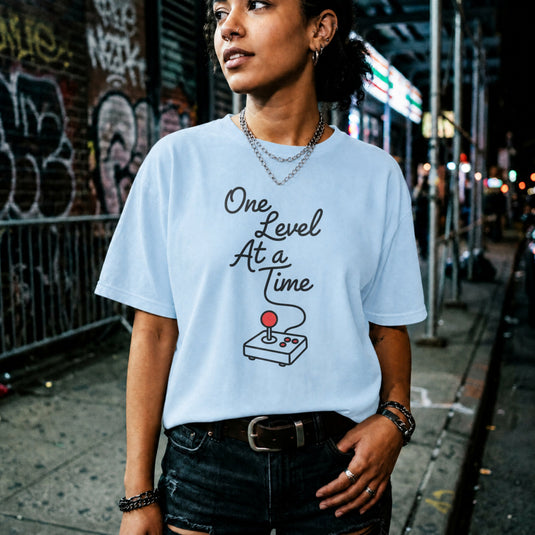 Translation missing: en.Light blue cotton tee with retro arcade joystick graphic and text "One Level At A Time"