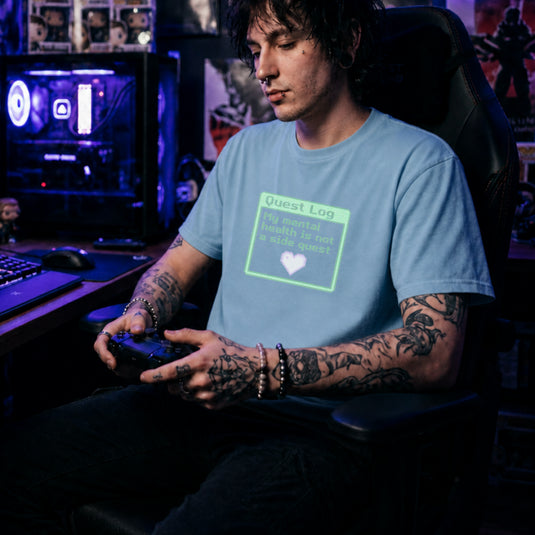 Translation missing: en.Light blue shirt with a green pixel art quest log graphic reading My mental health is not a side quest with a heart