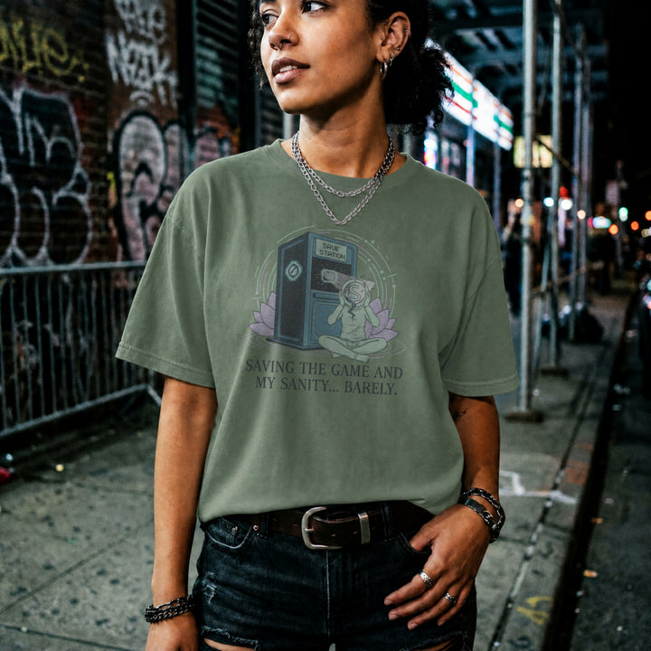 Translation missing: en.Military green tee with a meditating figure holding a cracked head by a Save Station. Text: Saving the game and my sanity