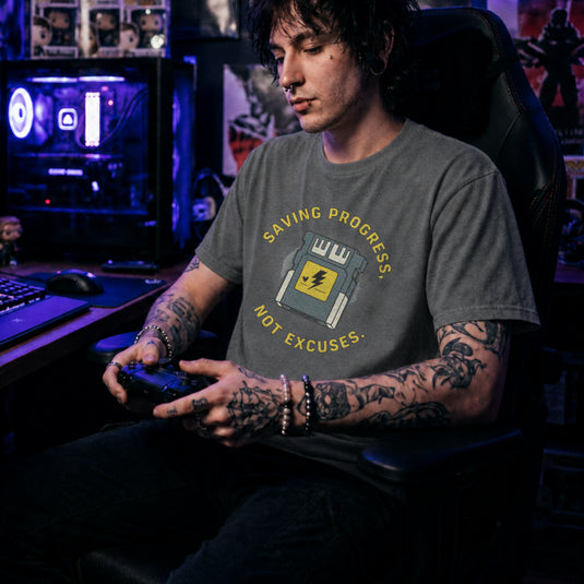 Translation missing: en.Graphite heather t-shirt with yellow text reading Saving Progress, Not Excuses around a retro console memory card icon