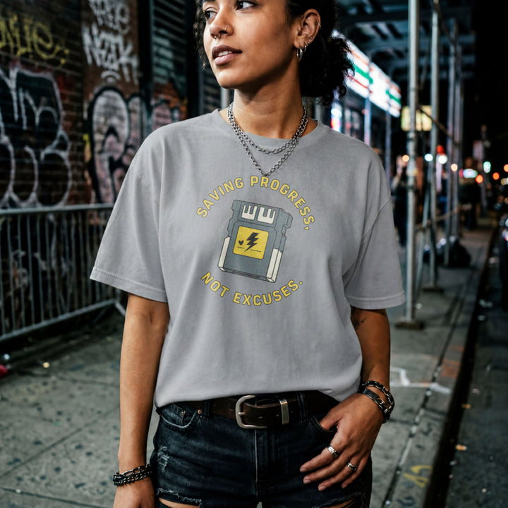 Translation missing: en.sports grey t-shirt with yellow text reading Saving Progress, Not Excuses around a retro console memory card icon
