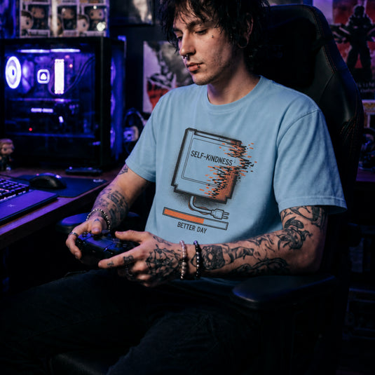 Translation missing: en.Light blue tee with a retro gaming cartridge labeled Self-Kindness glitching above a Better Day orange loading bar