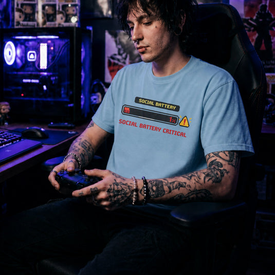 Translation missing: en.Light blue shirt with a pixel art one percent loading bar graphic and text reading Social Battery Critical