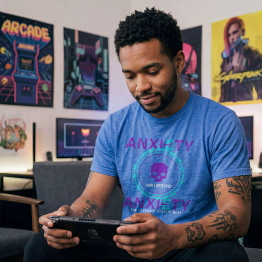 Translation missing: en.Purple and teal pixelated glitch text reading Anxiety Enemy Detected on a heather royal graphic gamer tee