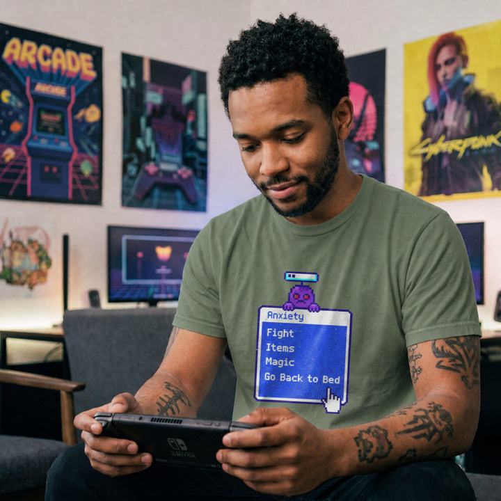 Translation missing: en.Military green t-shirt featuring a retro blue RPG battle menu box titled Anxiety with option Go Back to Bed