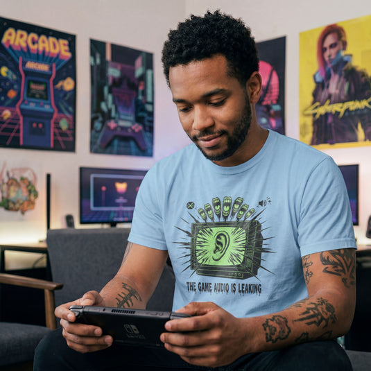 Translation missing: en.Light blue  t-shirt with a green retro TV displaying a large ear graphic and text reading THE GAME AUDIO IS LEAKING