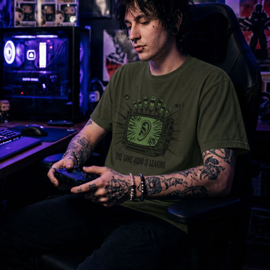Translation missing: en.Alt n Vibe military green t-shirt with a green retro TV displaying a large ear graphic and text reading THE GAME AUDIO IS LEAKING