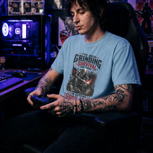 Translation missing: en.Light blue t-shirt with skeleton warrior sharpening sword on grindstone graphic and text: Grinding survival for years