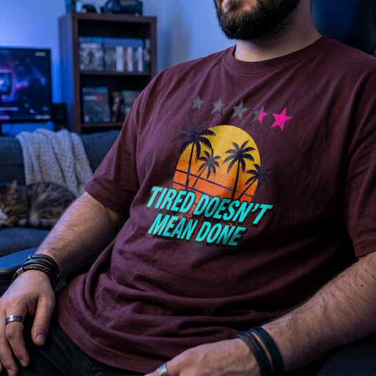 Translation missing: en.Maroon t-shirt with retro palm tree sunset graphic and text: Tired Doesn't Mean Done with 5-star rating graphic