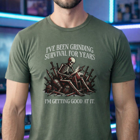 Translation missing: en.Military green t-shirt with skeleton warrior sharpening dagger on grindstone graphic and text: Grinding survival for years