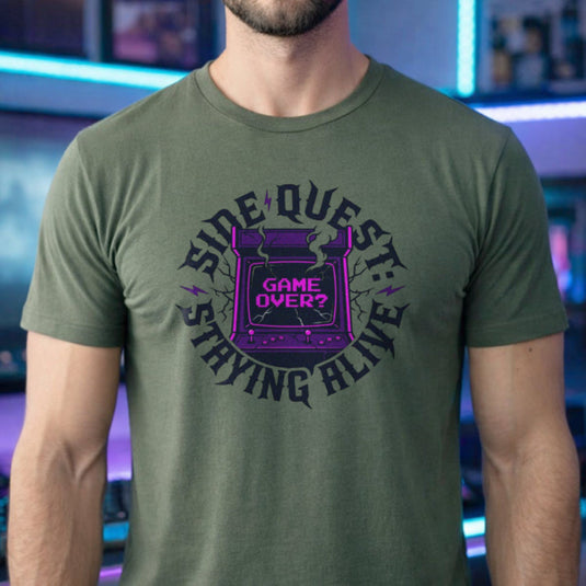 Translation missing: en.Military green t-shirt with cracked purple arcade cabinet, smoke, and text: Side Quest: Staying Alive, Game Over? graphic