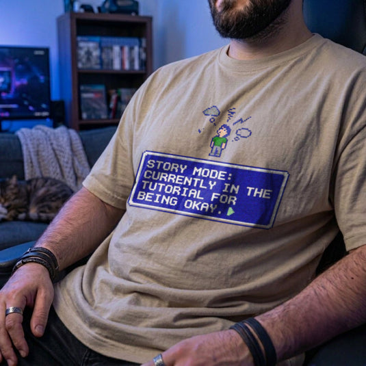 Translation missing: en.Sand t-shirt with pixel art character, thought cloud, and RPG text box: Story Mode tutorial for being okay