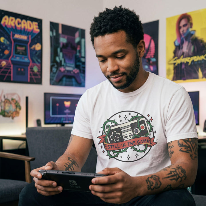 Translation missing: en.White  t-shirt with a classic retro controller tangled in green thorns and a banner reading STILL IN THE GAME. 