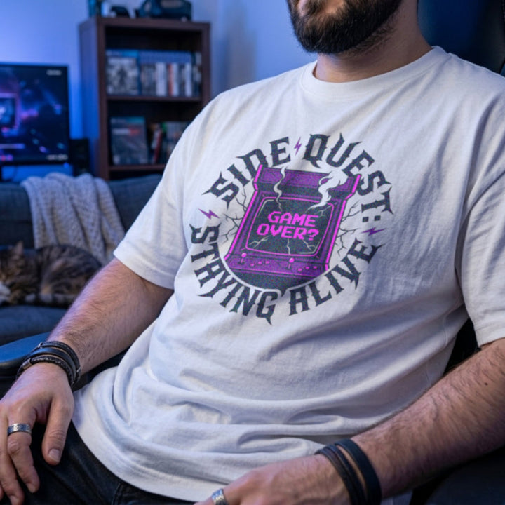 Translation missing: en.White t-shirt with cracked purple arcade cabinet, smoke, and text: Side Quest: Staying Alive, Game Over? graphic